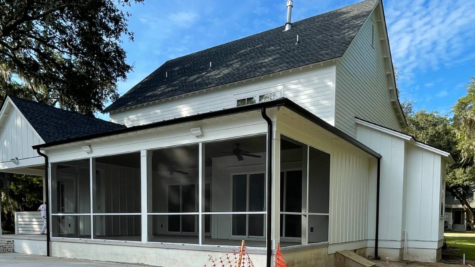 A white house with a screened in porch and a black roof with gutters.