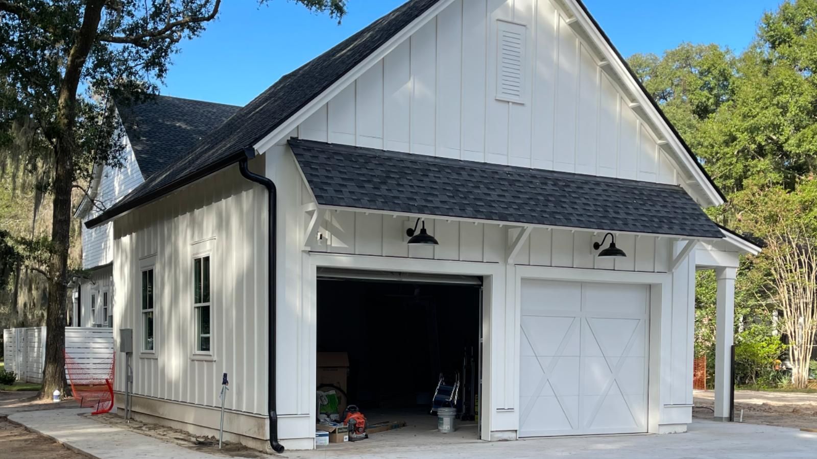 A white garage with a black roof and new gutters is sitting next to a house.