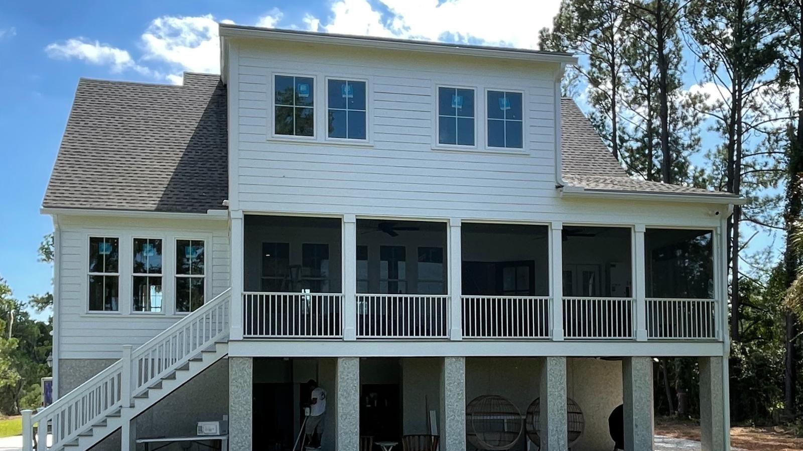 A large white house with a screened in porch and stairs after rain gutter installation.