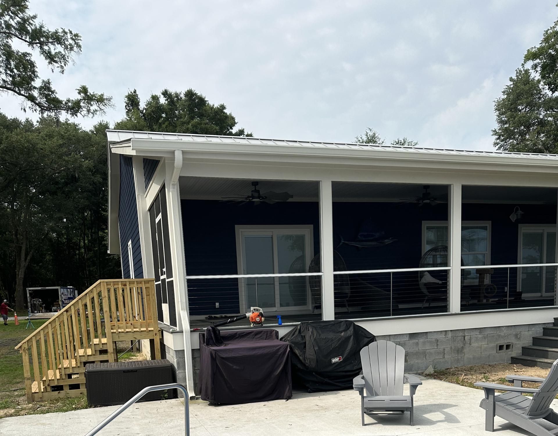 Small porch on a dark building with white columns, wooden steps, and outdoor furniture under cloudy sky.