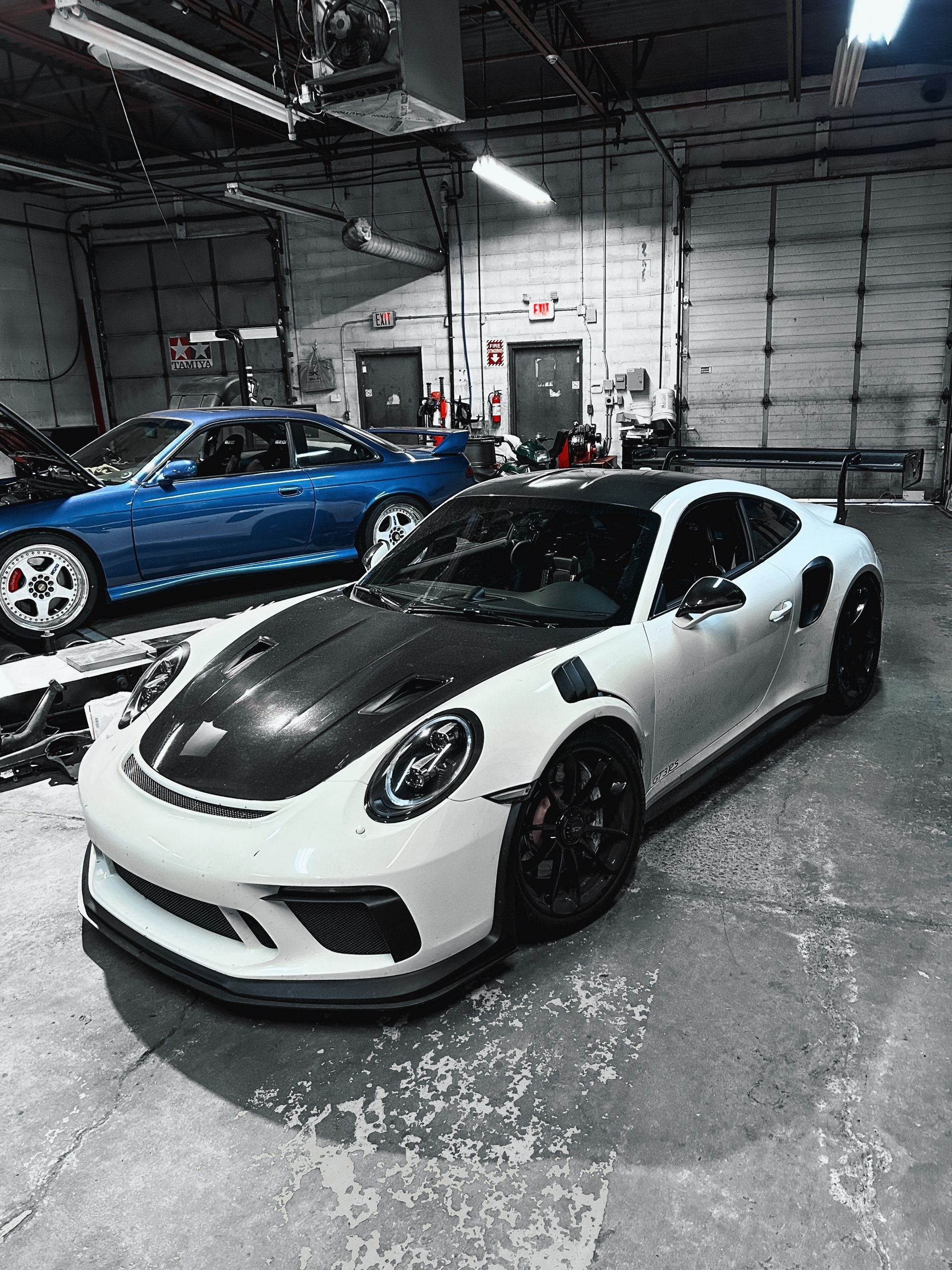 A white porsche 911 gt3 rs is parked in a garage next to a blue car.