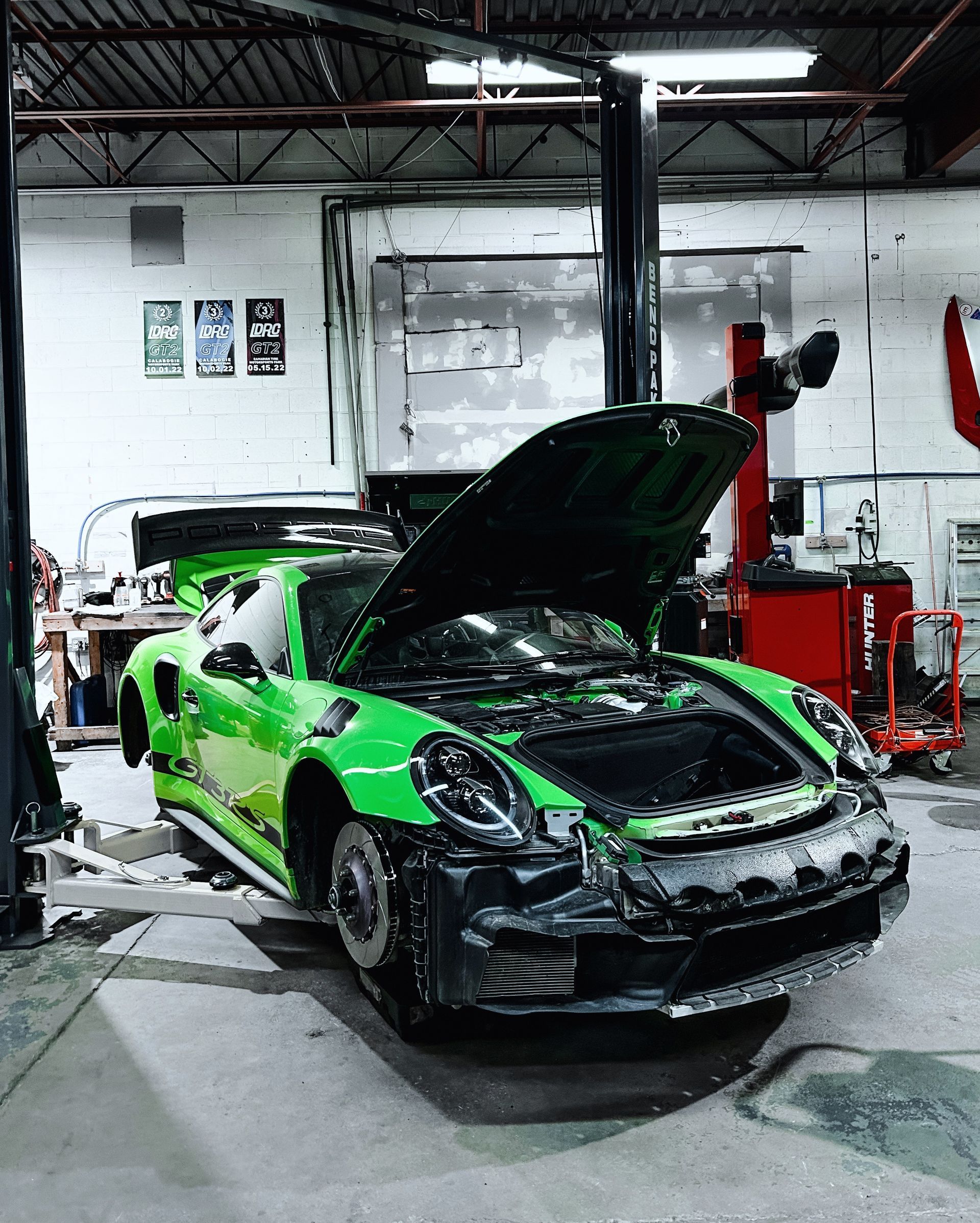 A green sports car is parked in a garage with its hood open.