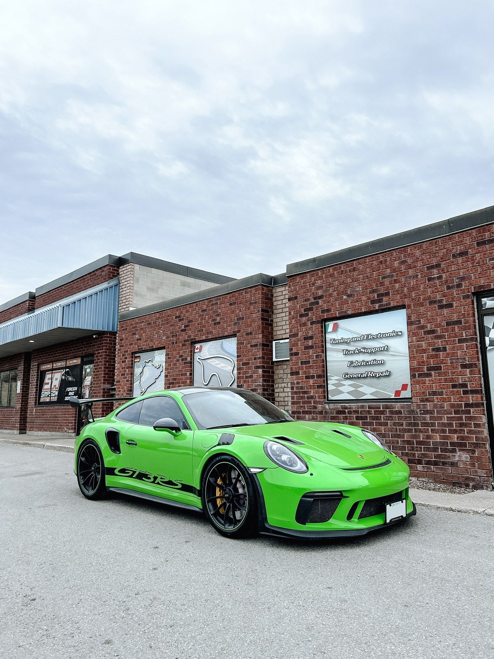 A green porsche 911 gt3 rs is parked in front of a brick building.