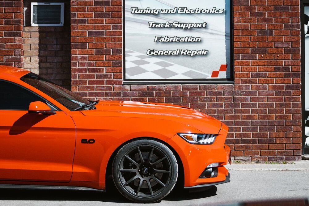 An orange mustang is parked in front of a brick building.