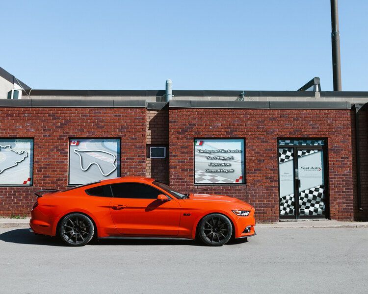 An orange mustang is parked in front of a brick building