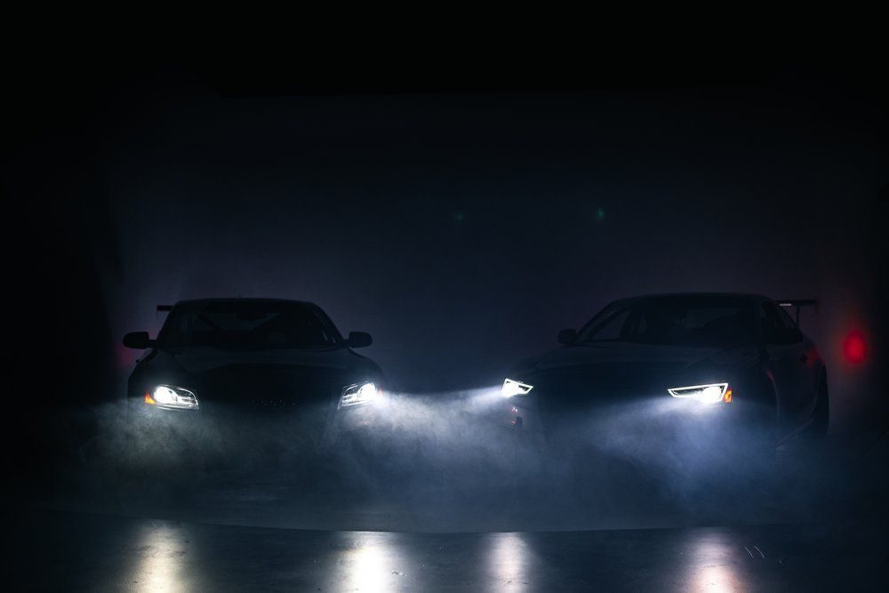 Two cars are driving in the dark with their headlights on.