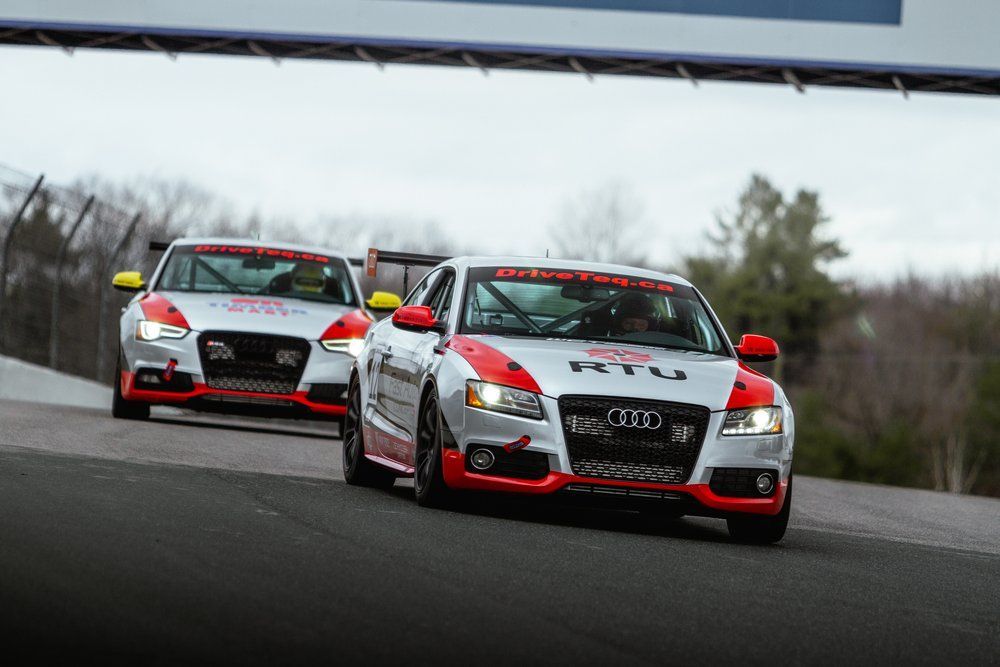 Two red and white race cars are driving down a track