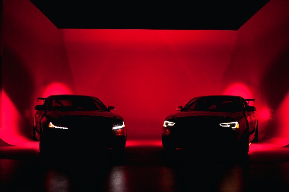 Two cars are parked next to each other in a dark room with red lights.
