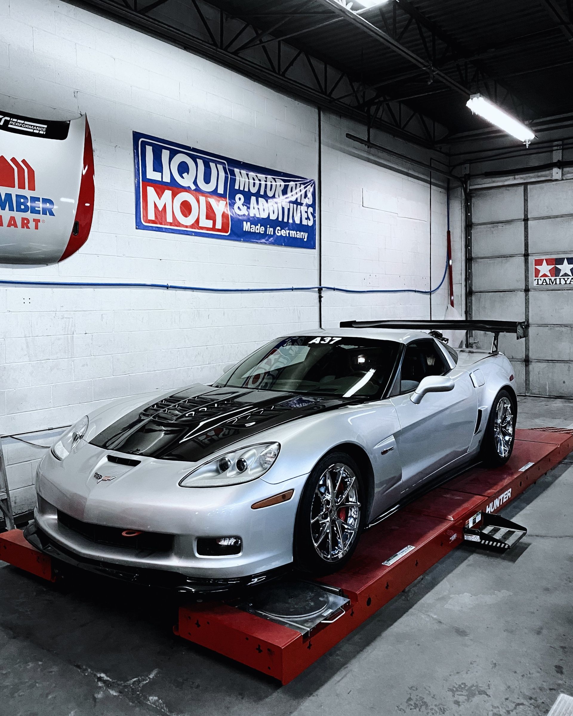 A silver sports car is on a ramp in a garage with a sign that says liqui moly