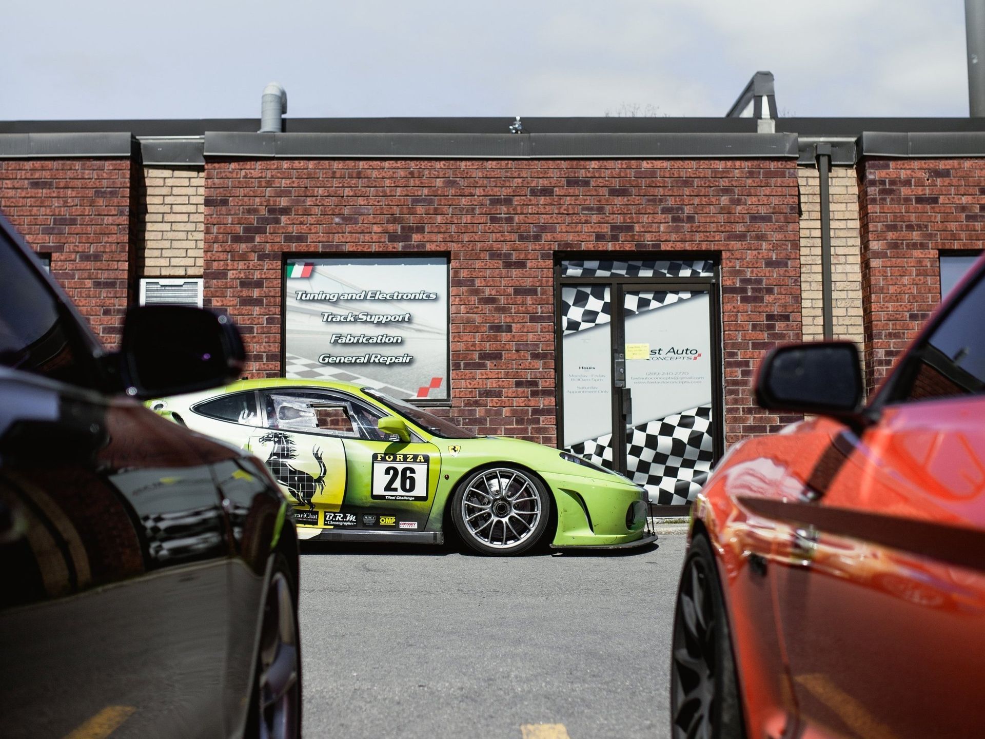 A green car with the number 26 on the side is parked in front of a brick building