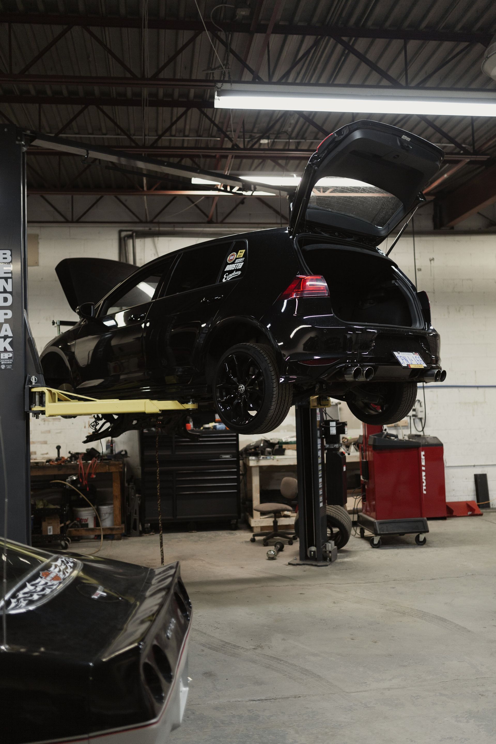 A black car is on a lift in a garage with the trunk open