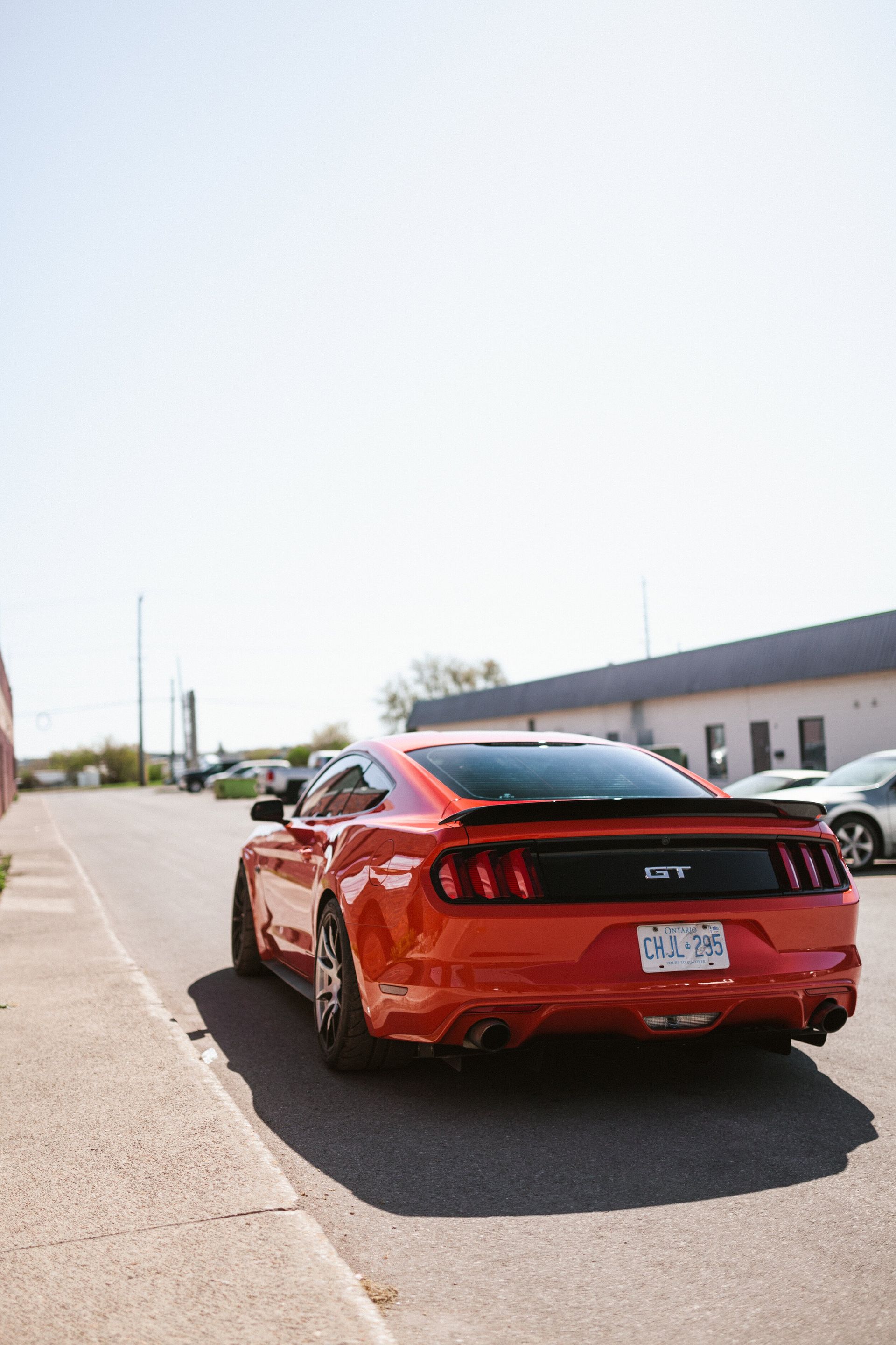 A red mustang is parked in a parking lot next to a building.
