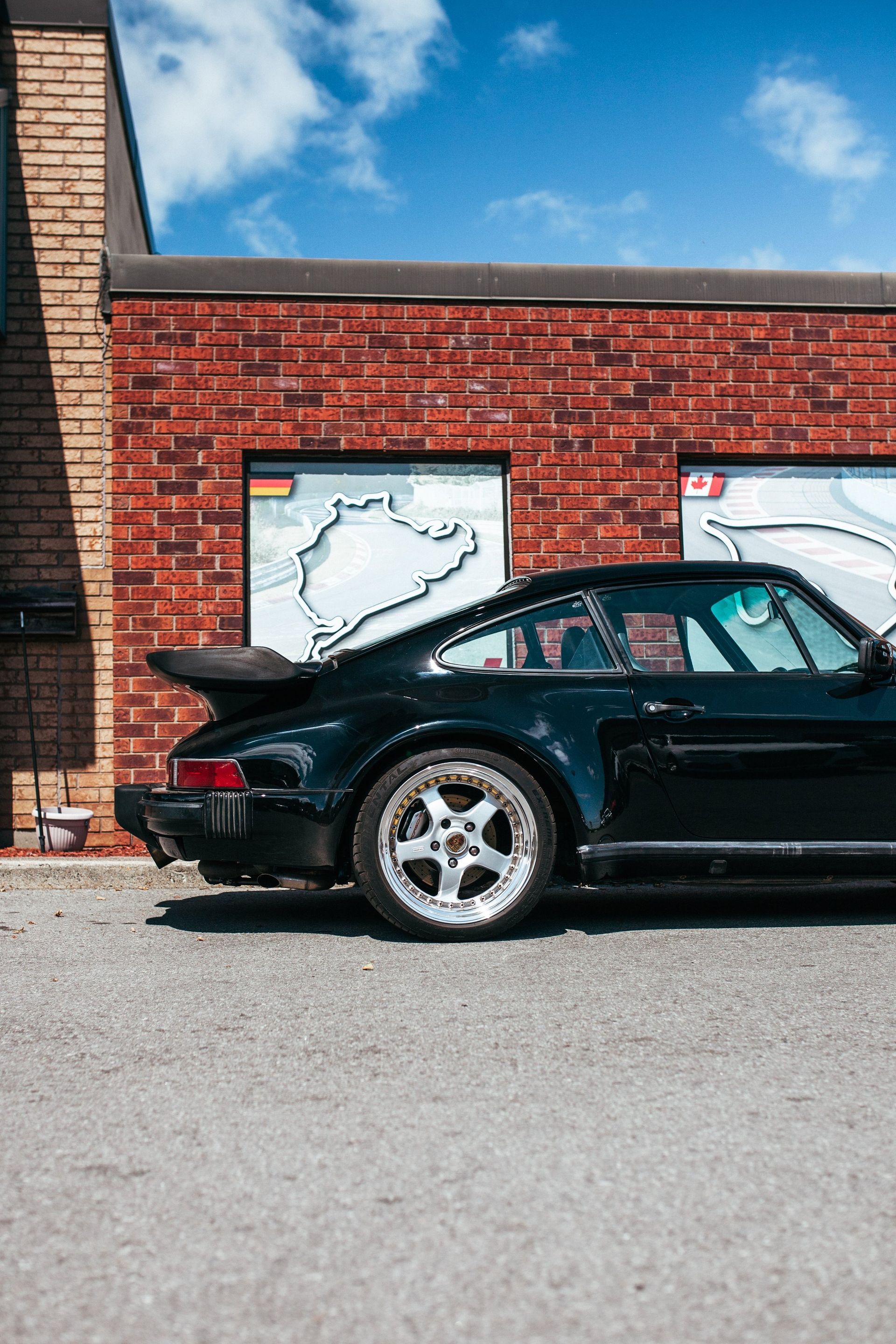 A black porsche 911 turbo is parked in front of a brick building.