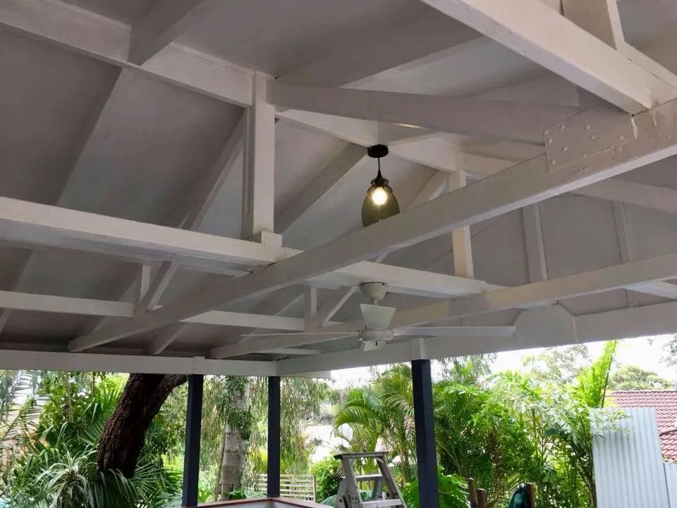 White Exposed Rafters and Beams Support a Sloped Roof Over an Outdoor Patio — Technik Electrical in Renwick, NSW