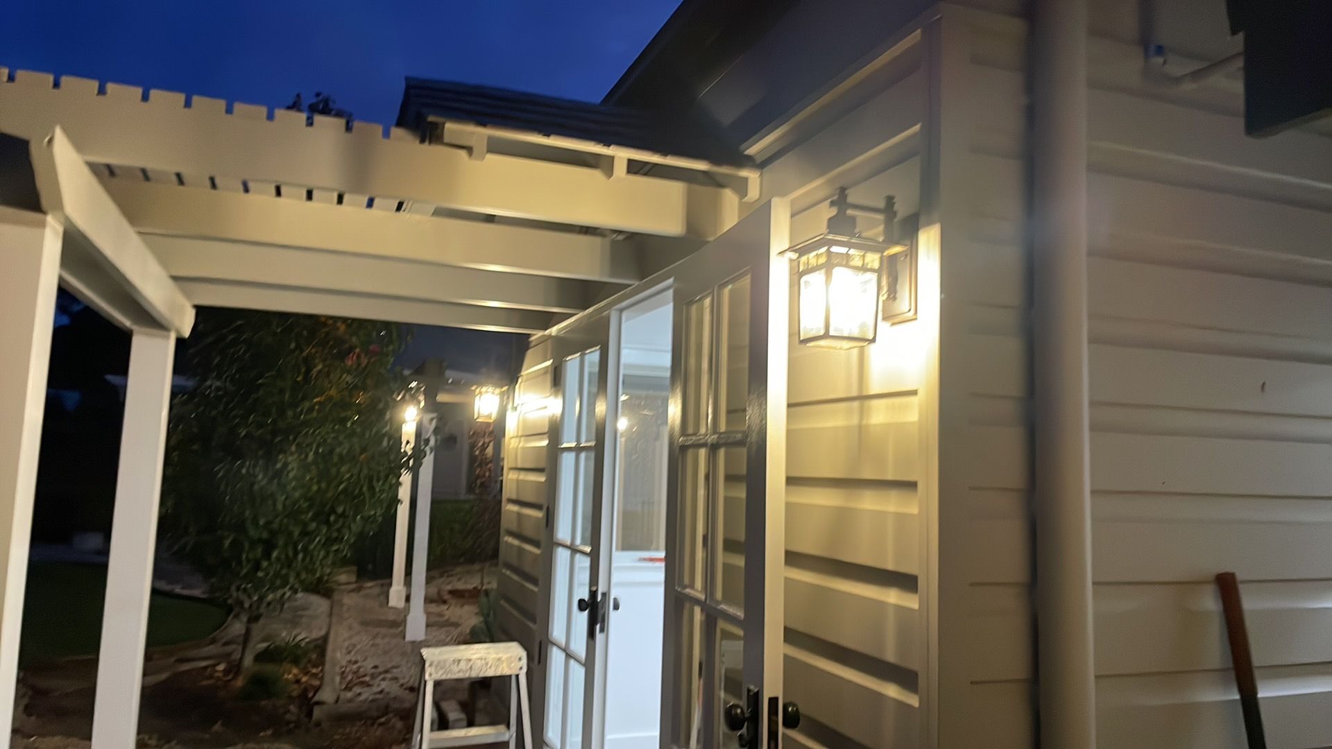 Side of a house at night with lit porch lights, white siding, sliding door, and a small stool on the patio — Technik Electrical in Bowral, NSW