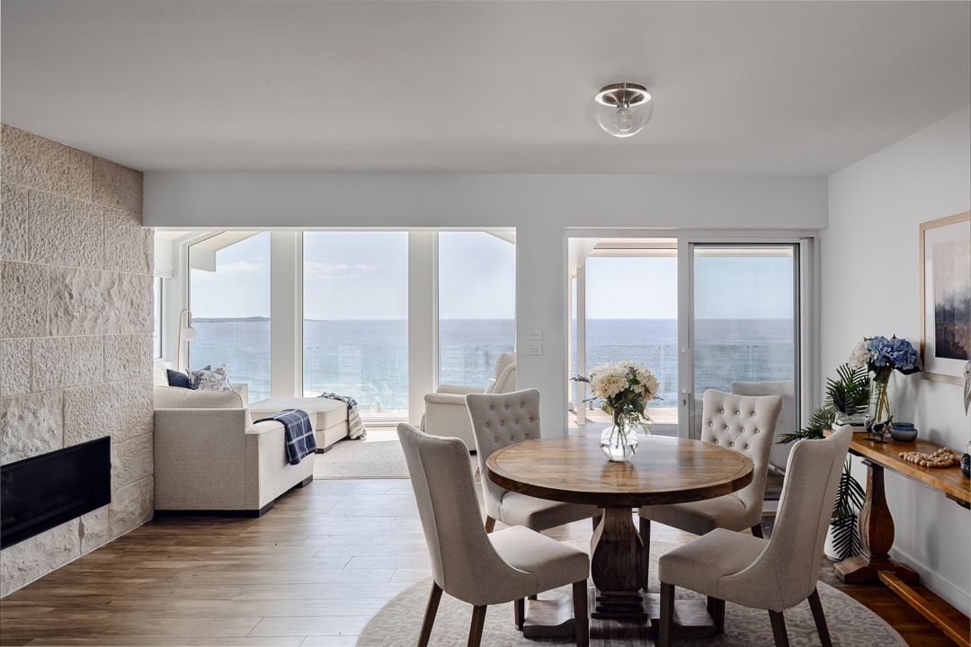 Bright modern living and dining room with ocean view, beige furniture, fireplace, and large windows. — Technik Electrical in Mittagong, NSW