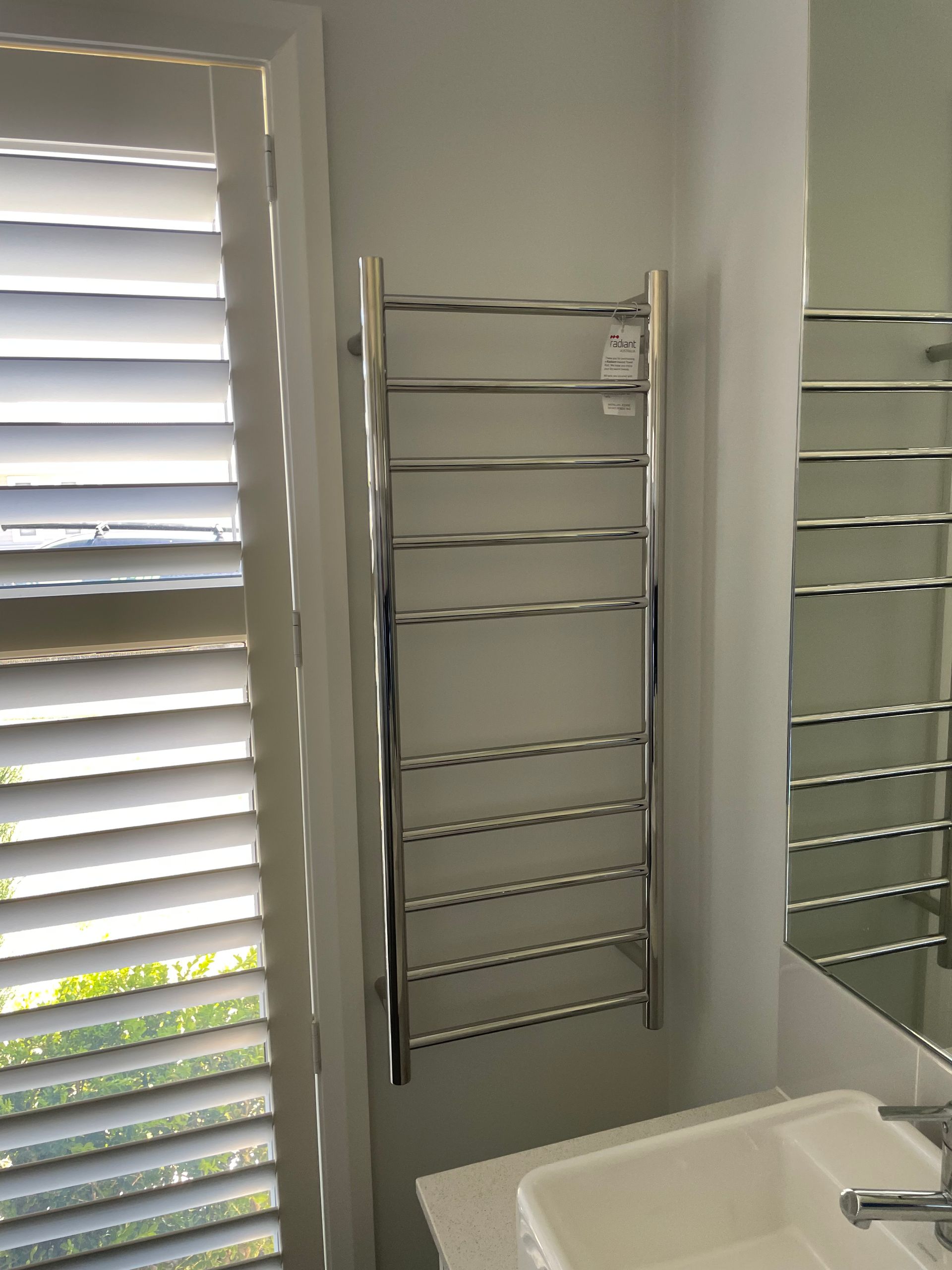 Bathroom with white shutters, a chrome towel rack, and a sink beside a mirror. — Technik Electrical in Renwick, NSW