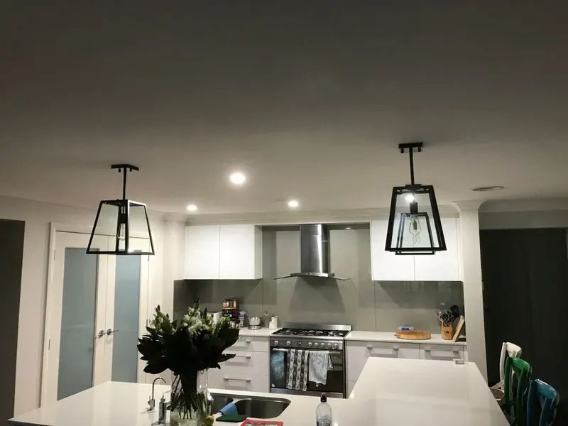 A Modern Kitchen Island With Two Black Lantern-style Pendant Lights Hanging — Technik Electrical in Renwick, NSW