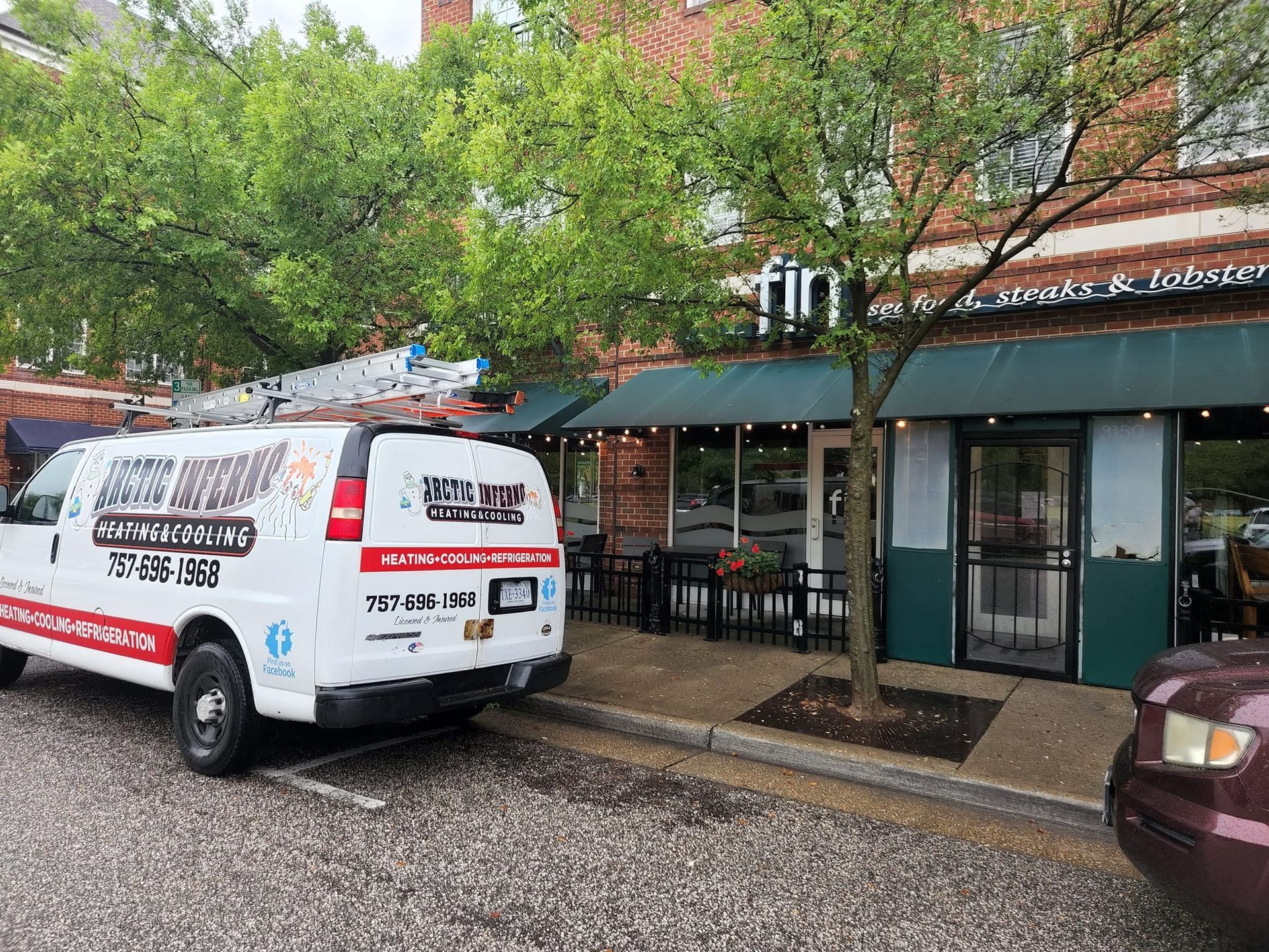 Van parked near restaurant, ladder on roof. Restaurant has green awning, outdoor seating, brick facade.