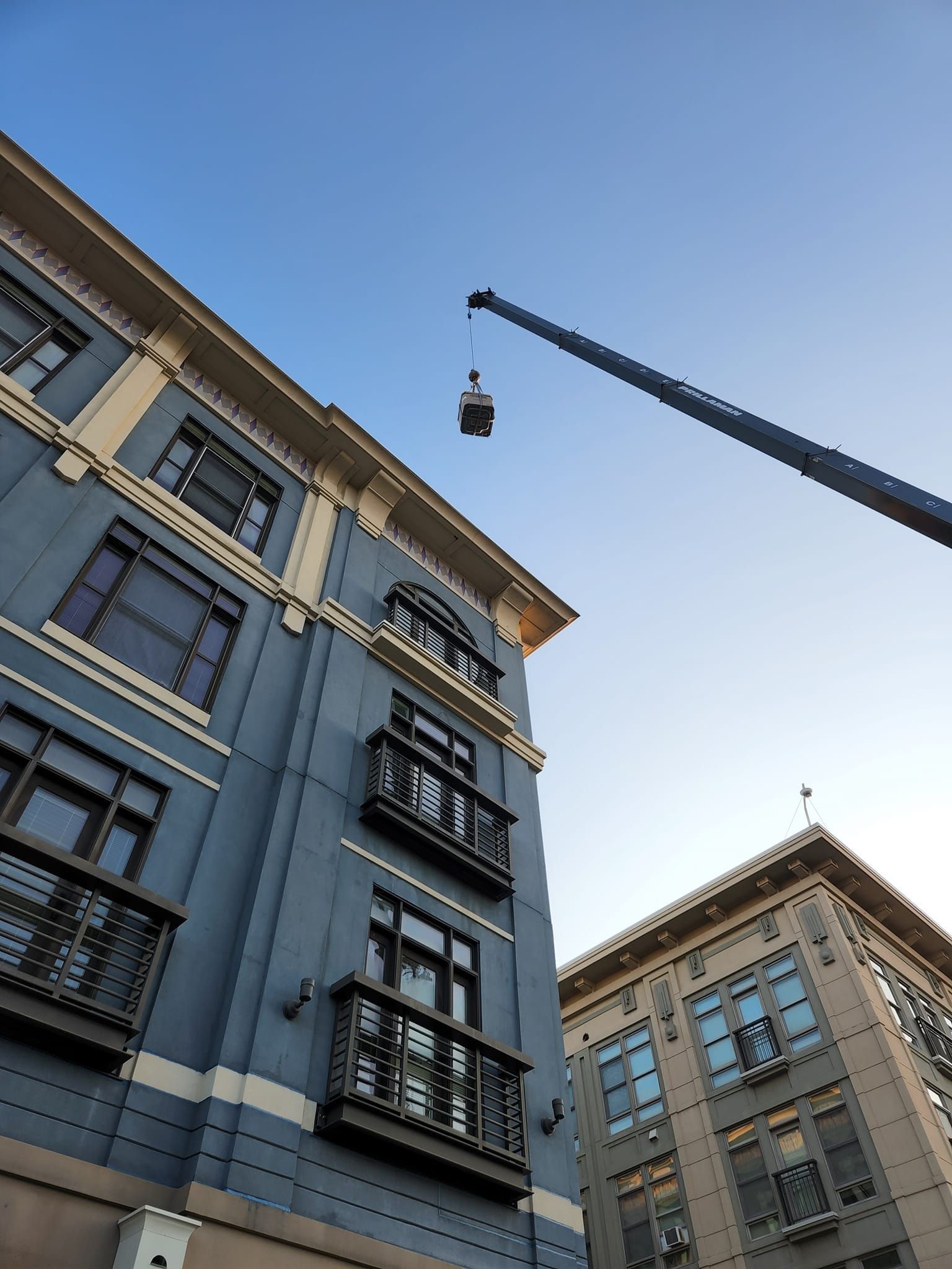 Buildings with balconies and a crane against a blue sky.