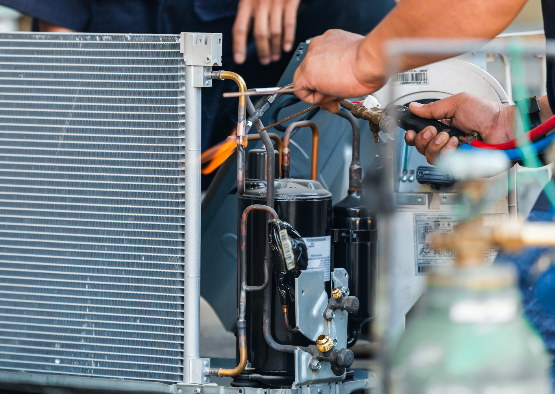 Hands of a technician repairing an AC unit, using tools on copper pipes.