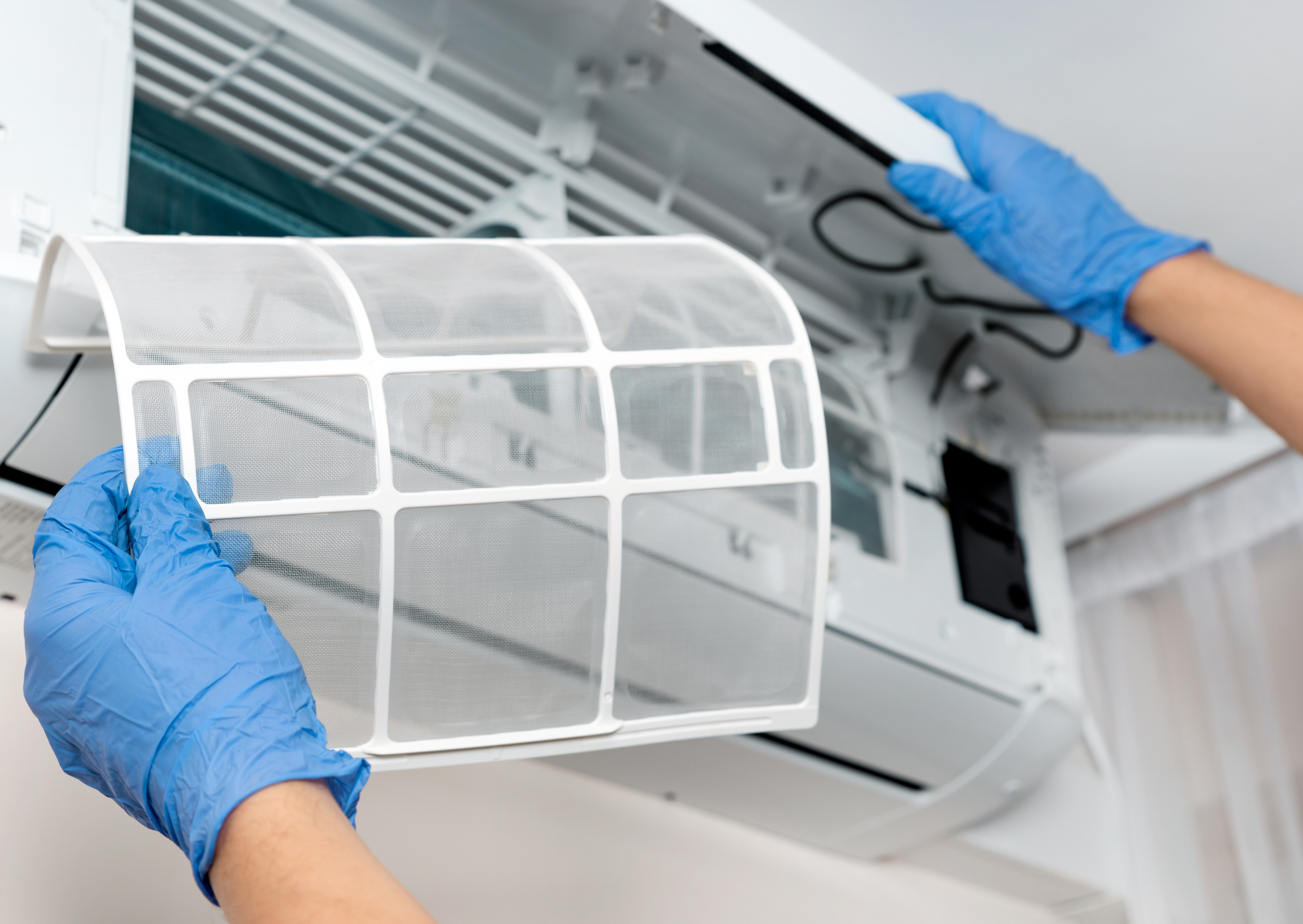 Person wearing blue gloves removing an air conditioner filter from a wall unit.