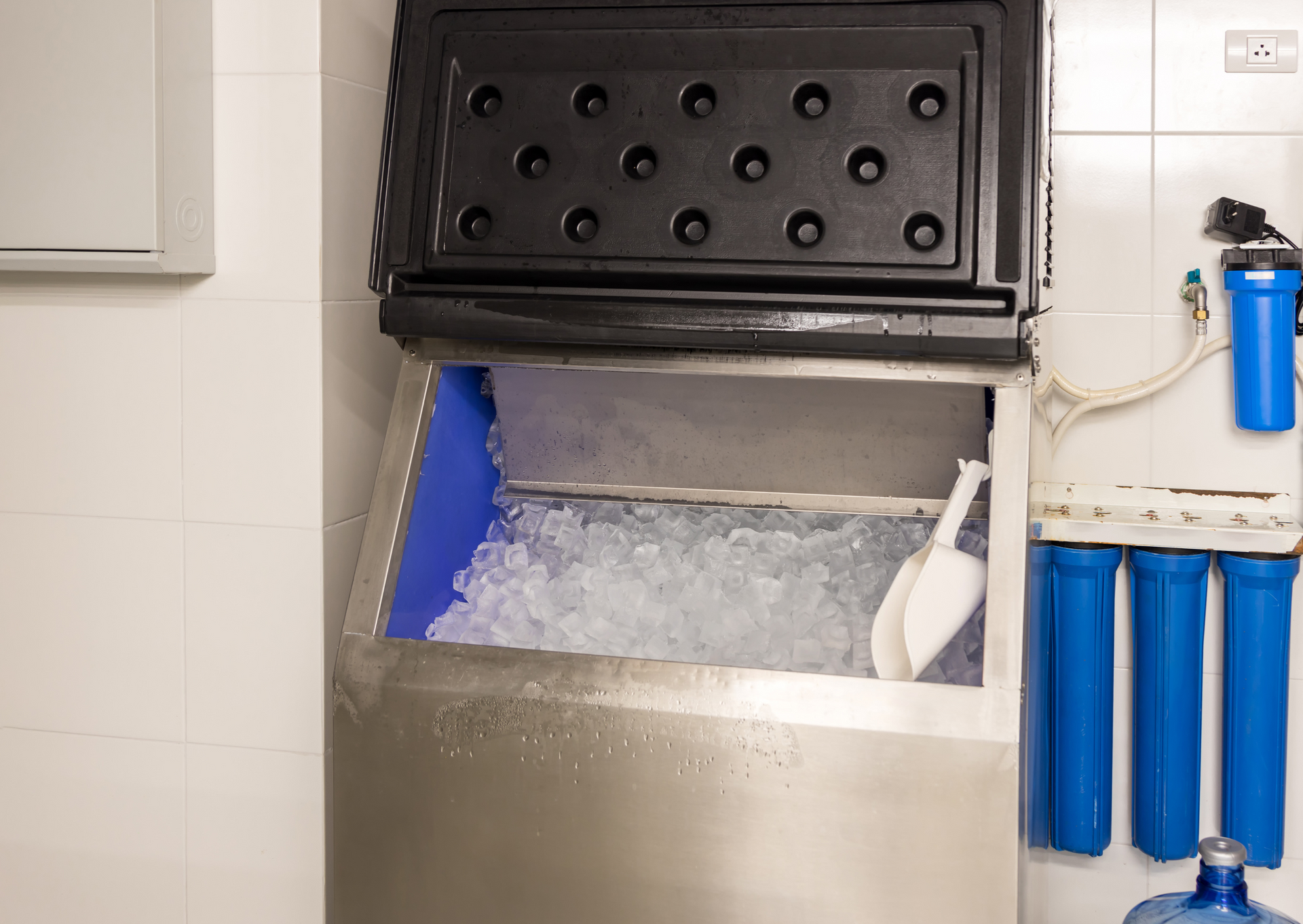 Ice machine with open bin full of ice, and a water filter system next to it.