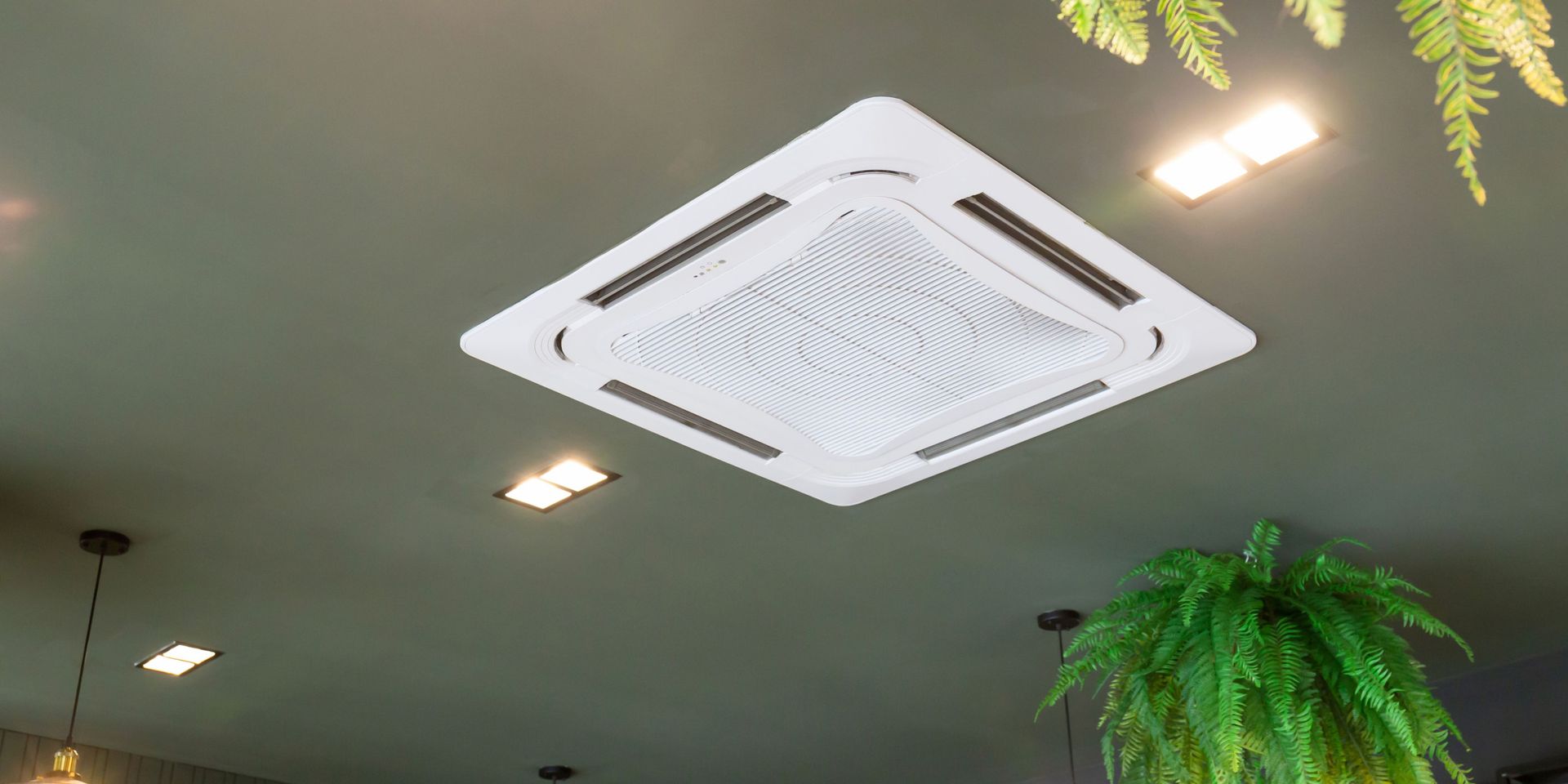 Ceiling-mounted air conditioner in a room with green ceiling and plants.