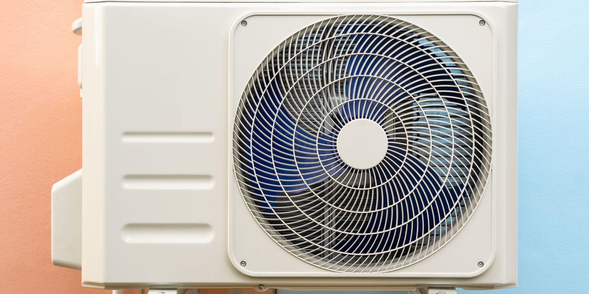 An air conditioning unit on a two-toned wall. A fan is visible behind a wire grill.