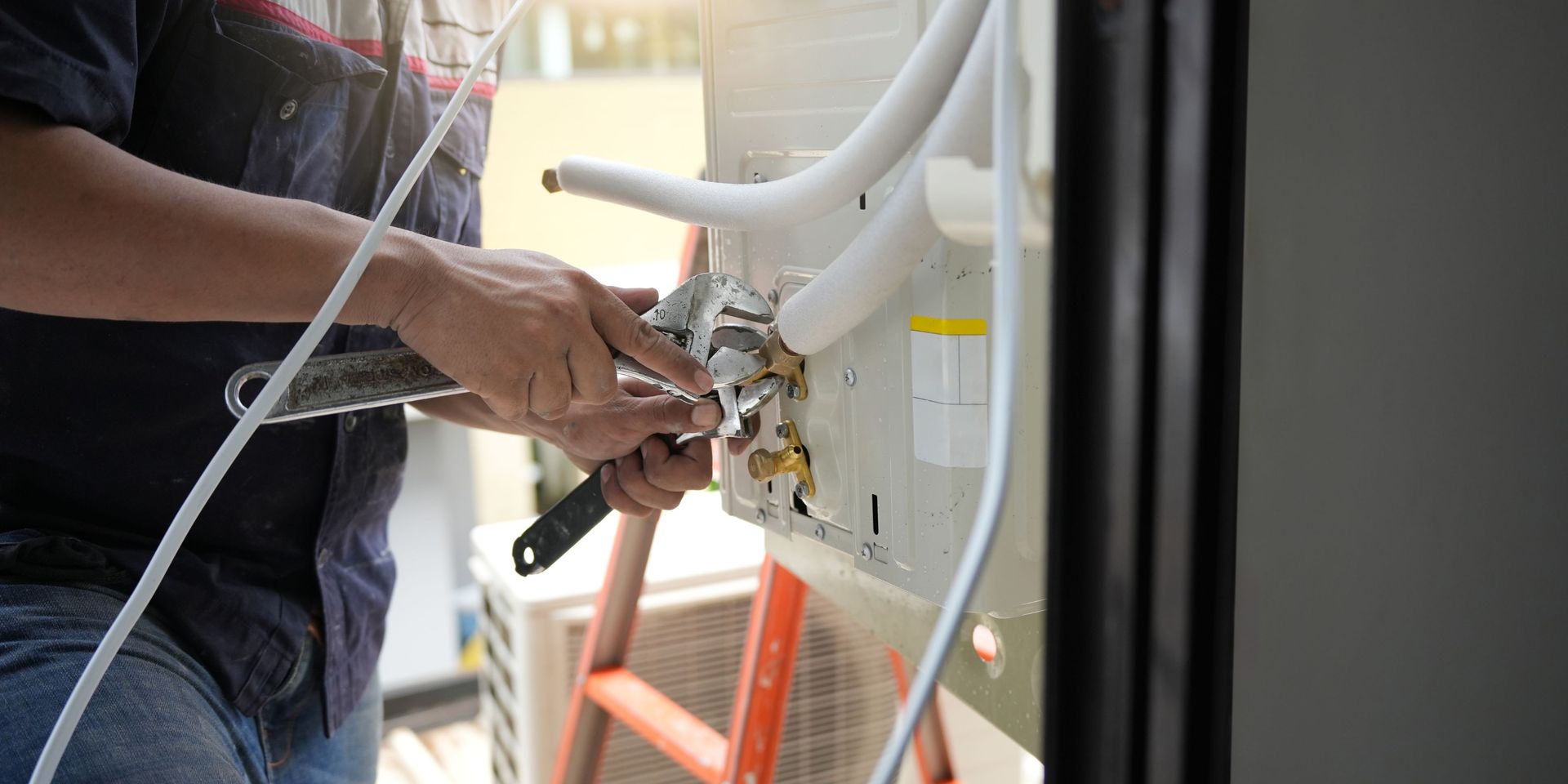 A person using a wrench to work on an air conditioning unit outside.
