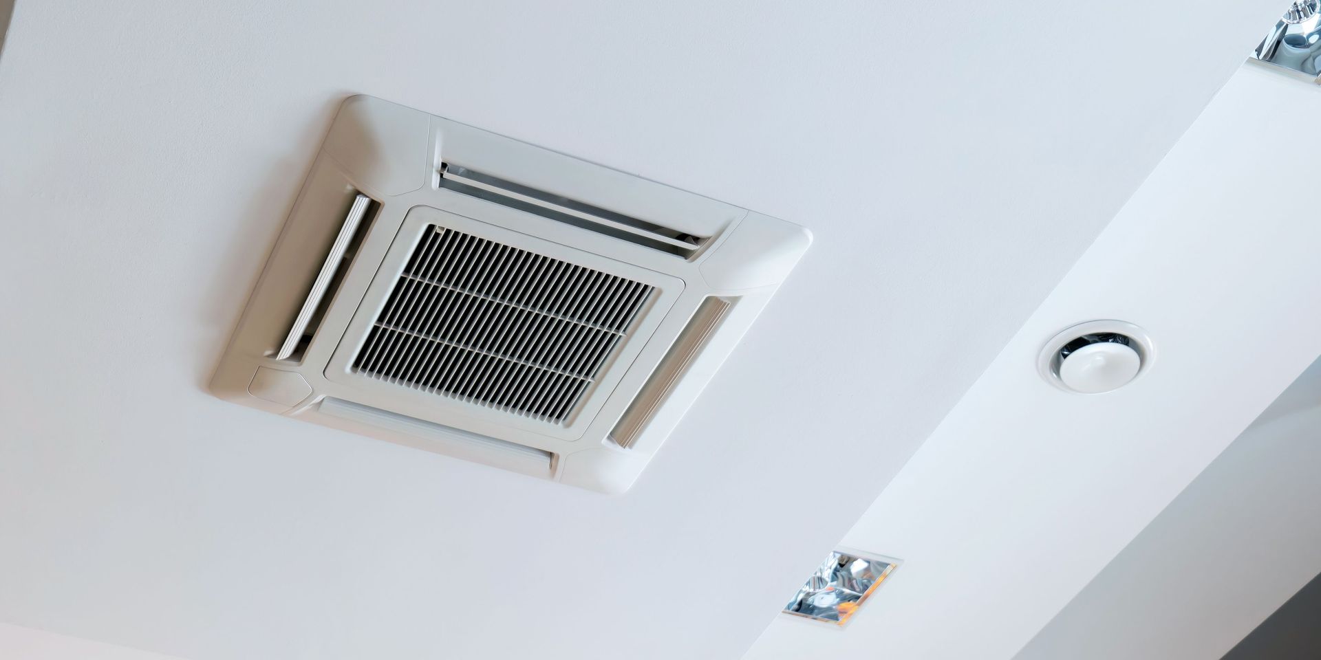 Ceiling-mounted air conditioner with a white ceiling, recessed lights, and vents.