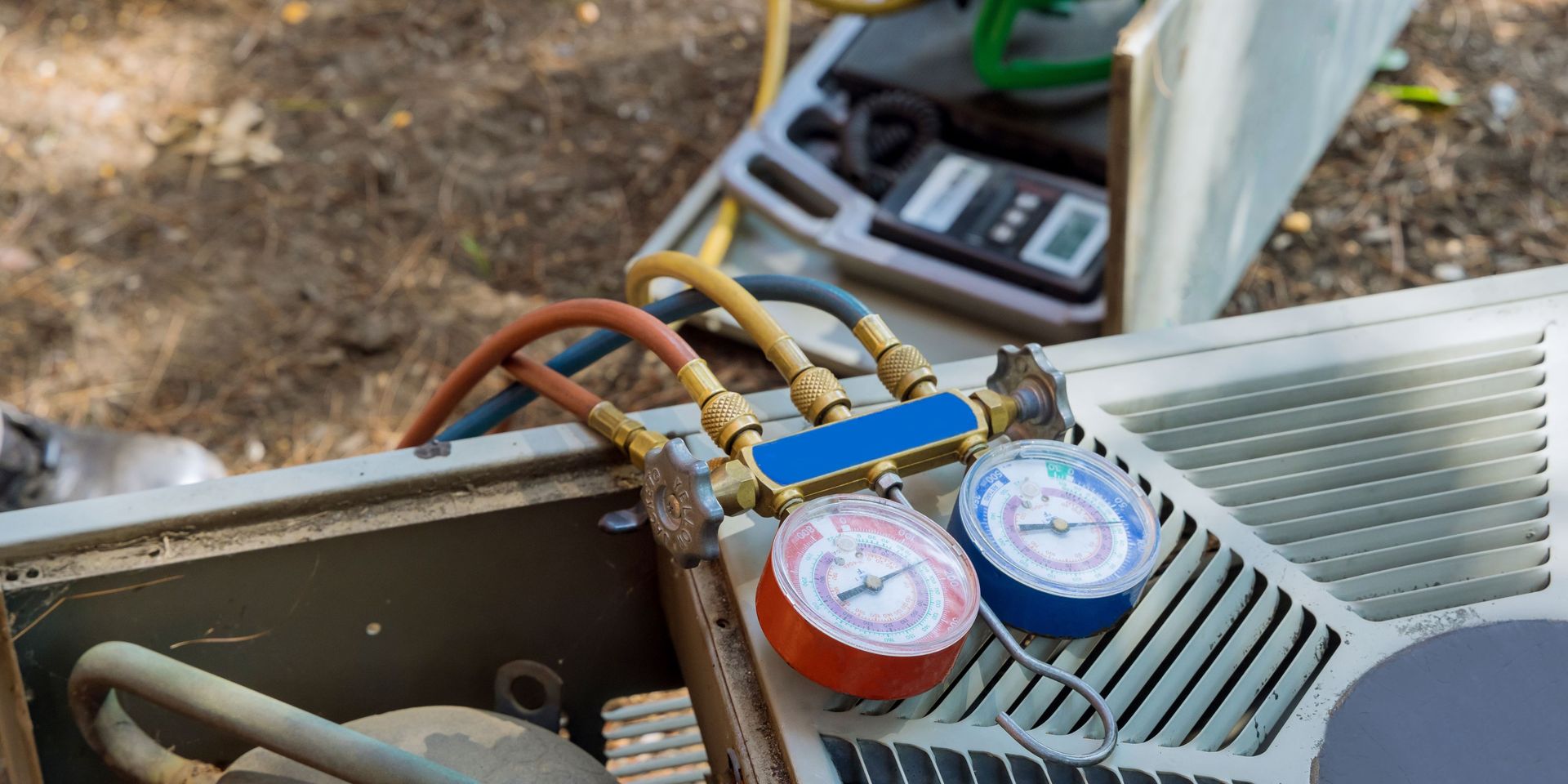 HVAC technician working on an air conditioning unit. Red and blue gauges attached with hoses.