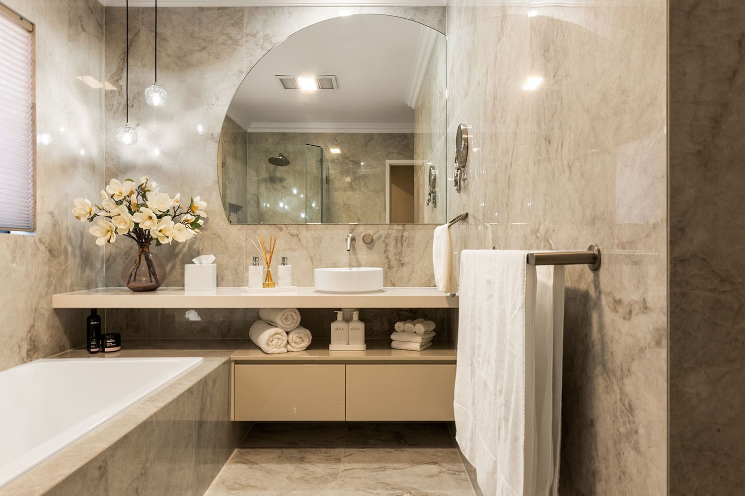Modern bathroom with marble walls, a large curved mirror, and a soaking tub.