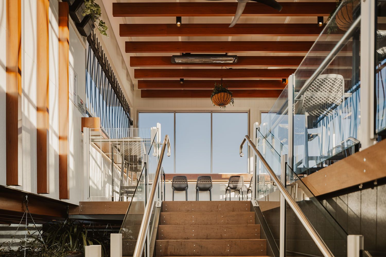 Staircase leading up to a window with chairs, brown ceiling beams, and a railing on both sides.