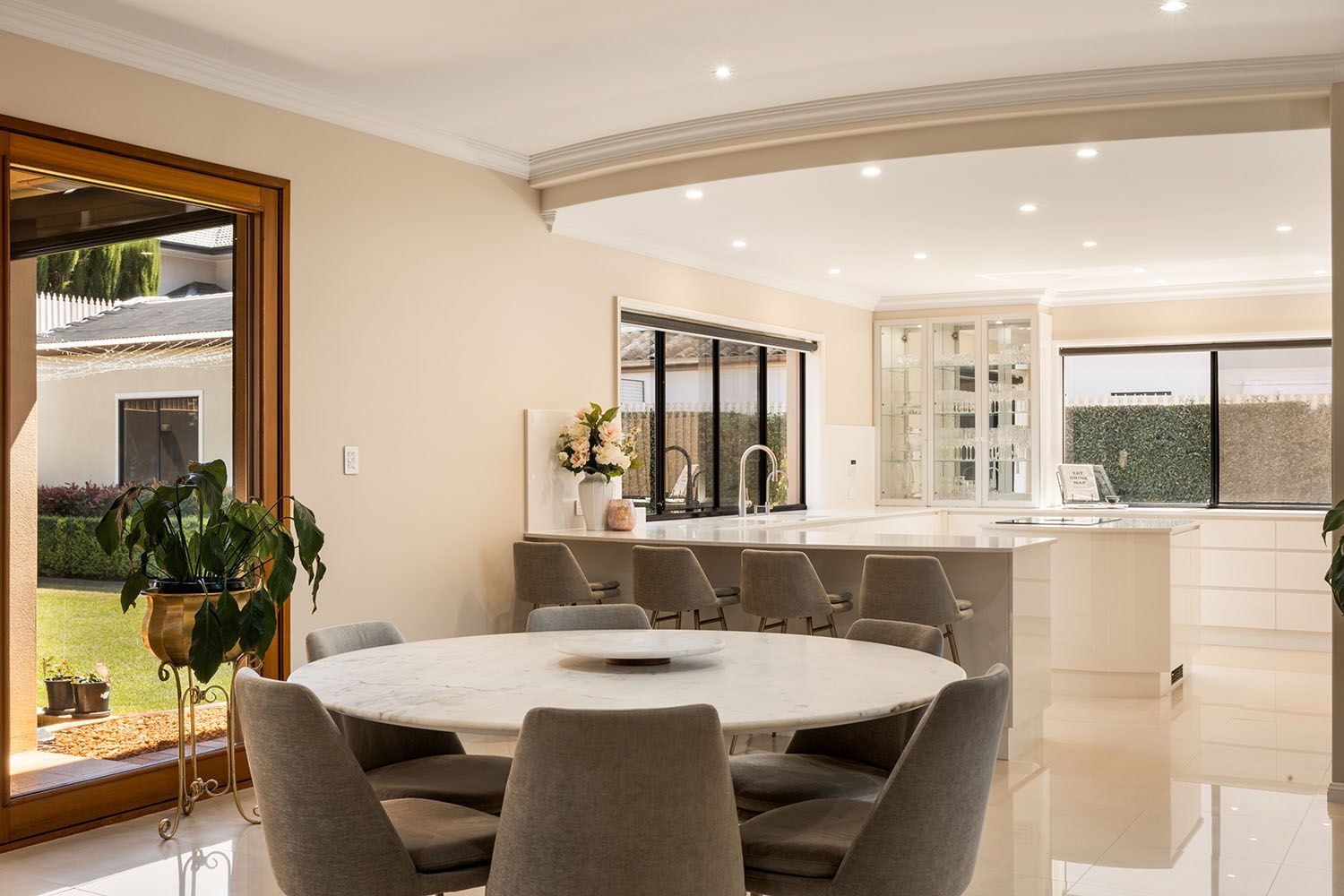 Dining room with a round marble table, gray chairs, and a kitchen in the background.