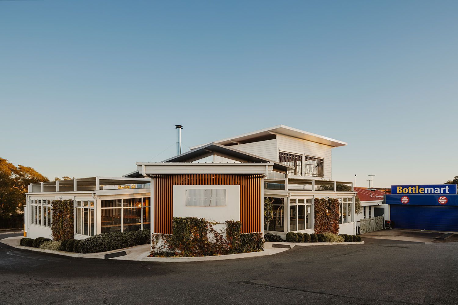 White building with a brown wooden section, covered with vines, against a clear sky.