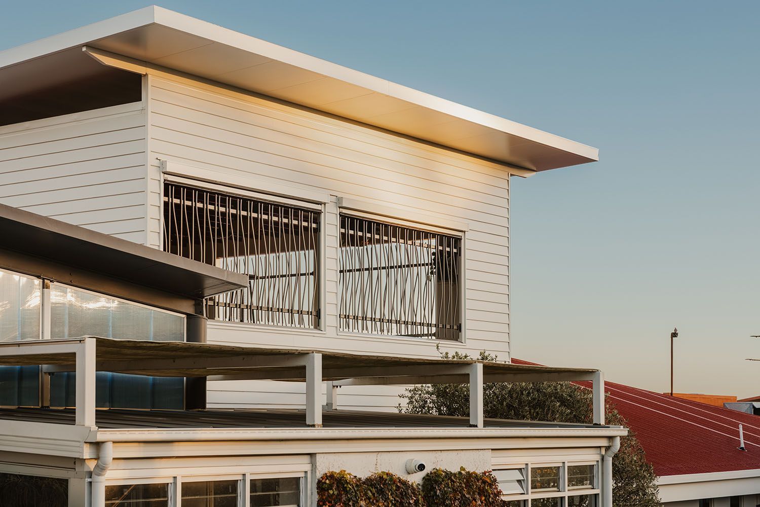 White two-story house with flat roof, balcony, and security bars on windows. Sunny day.