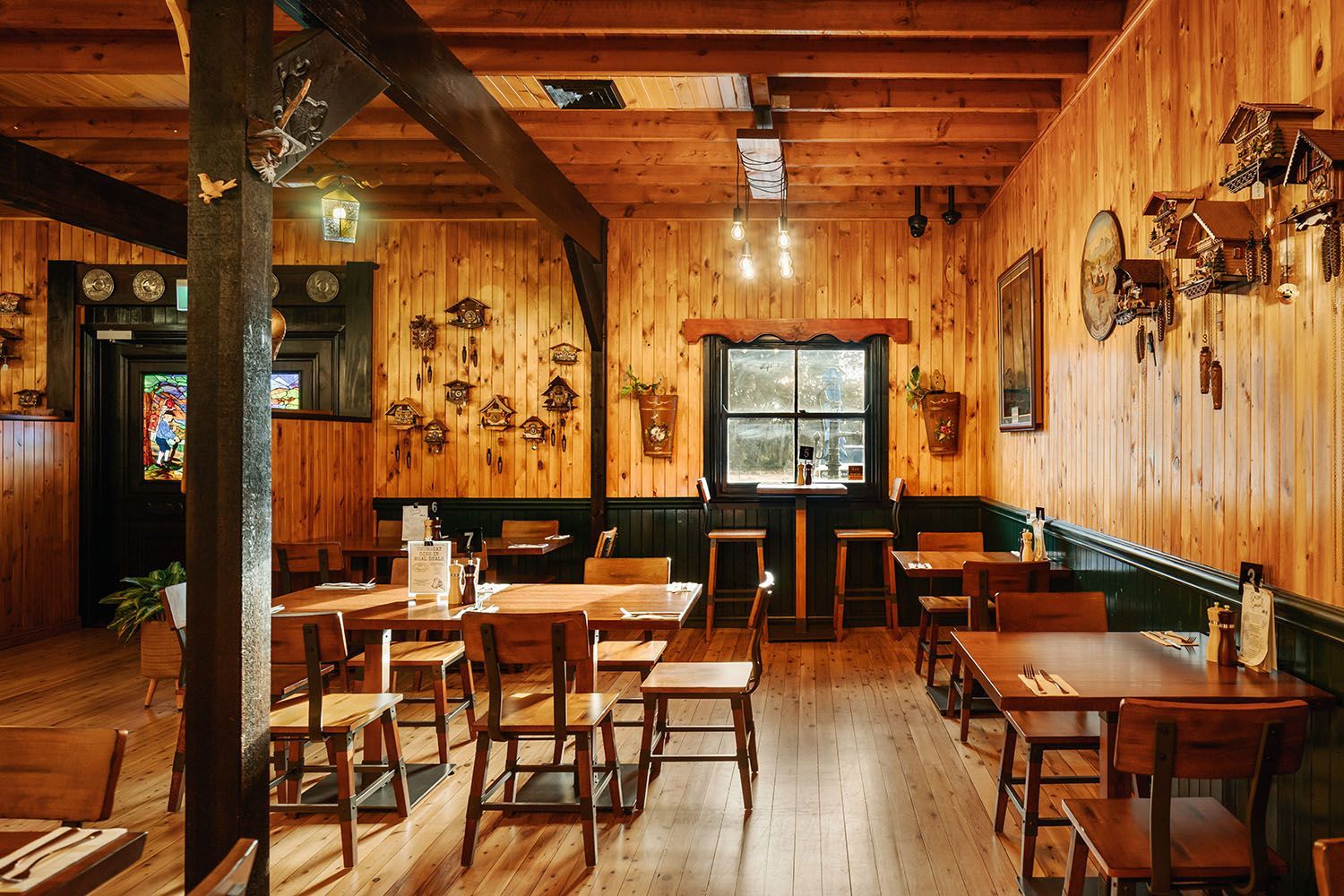 Wooden-walled restaurant interior with tables, chairs, and cuckoo clocks on the walls.