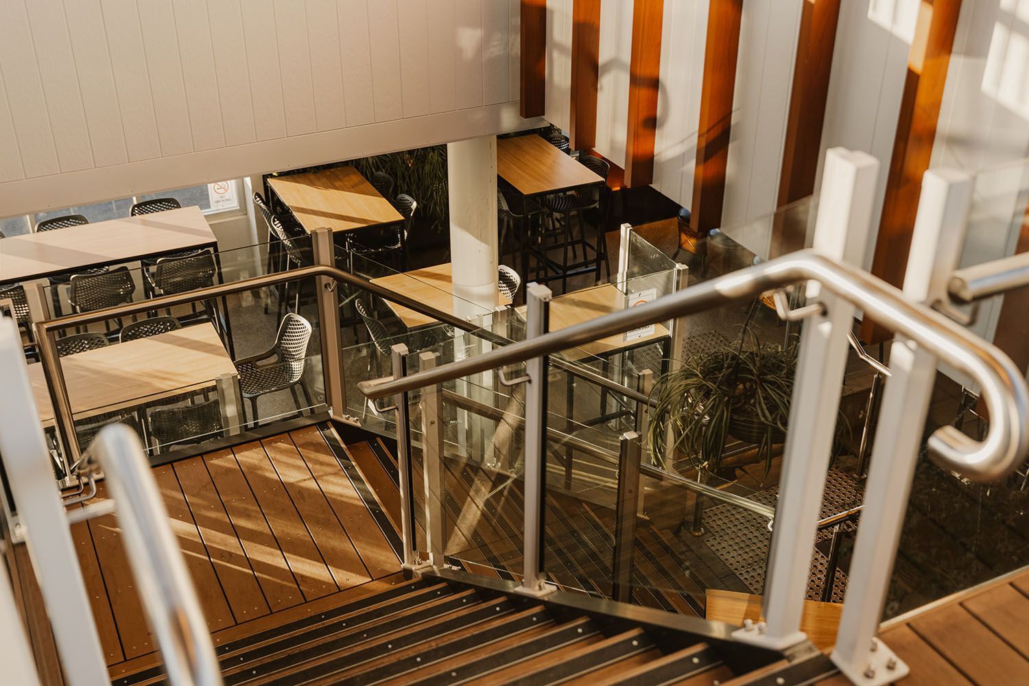 Staircase leading down to an outdoor dining area with tables and chairs. Striped wall and handrails.