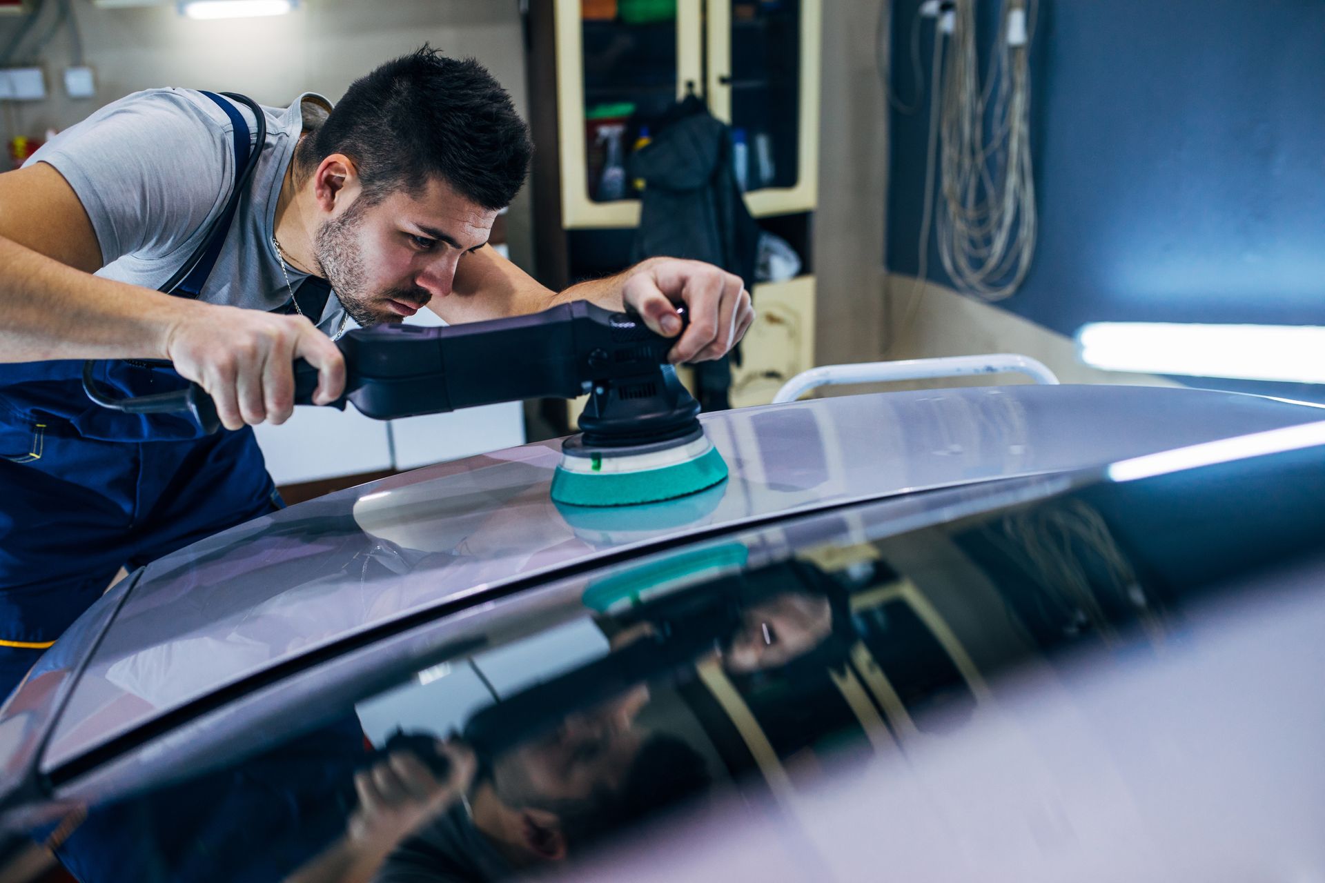 A man is polishing the roof of a car in a garage.