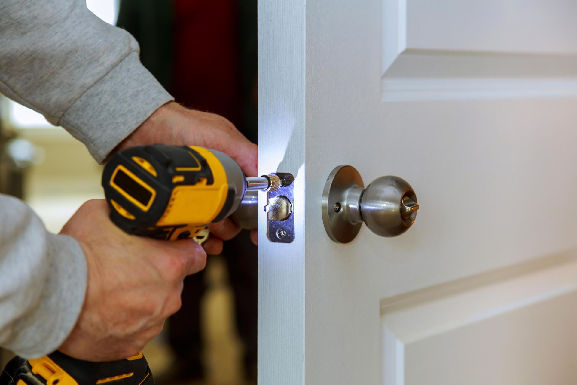 Person using a yellow drill to install a silver door lock on a white door