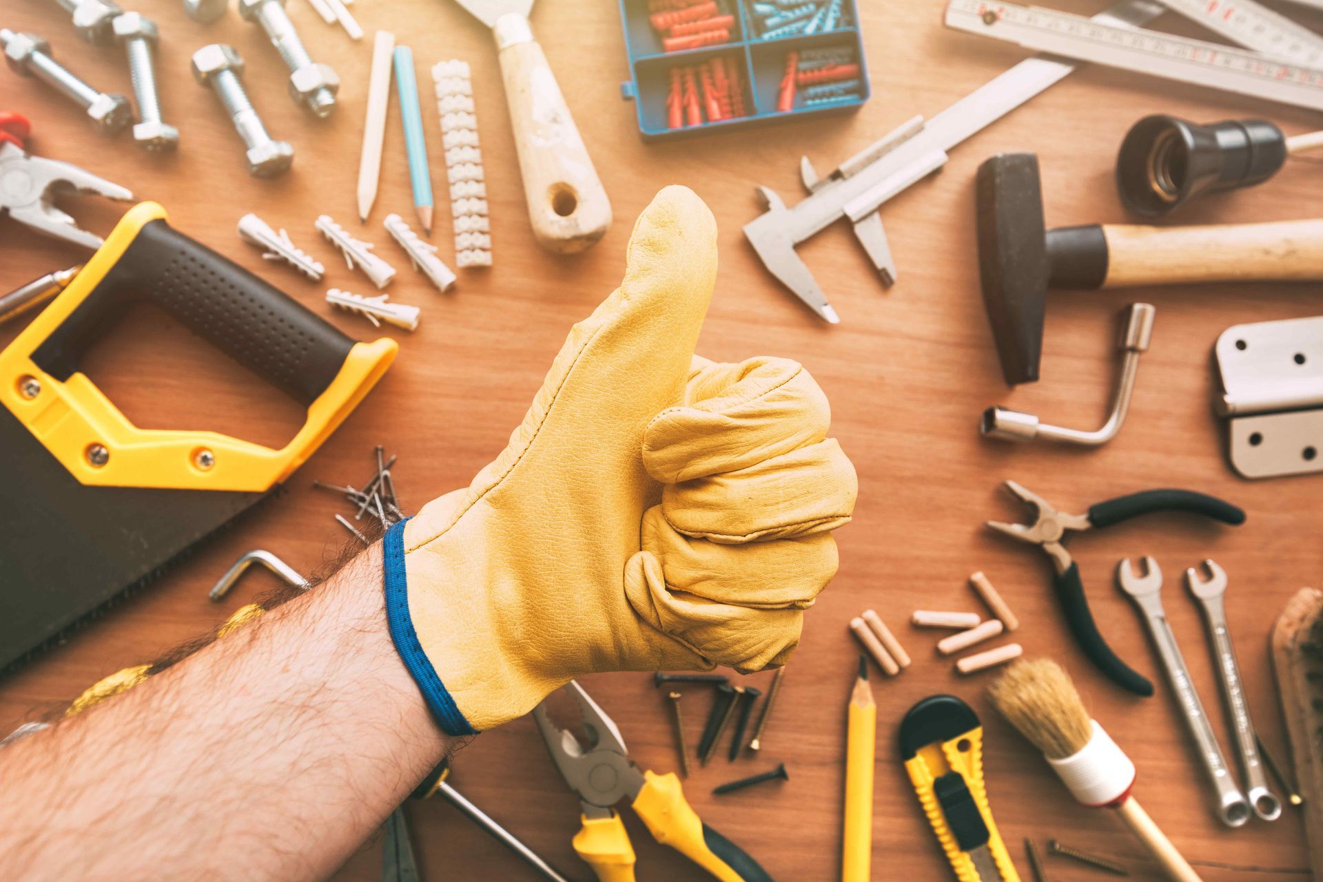 Gloved hand giving thumbs up over scattered hand tools on a wooden workbench