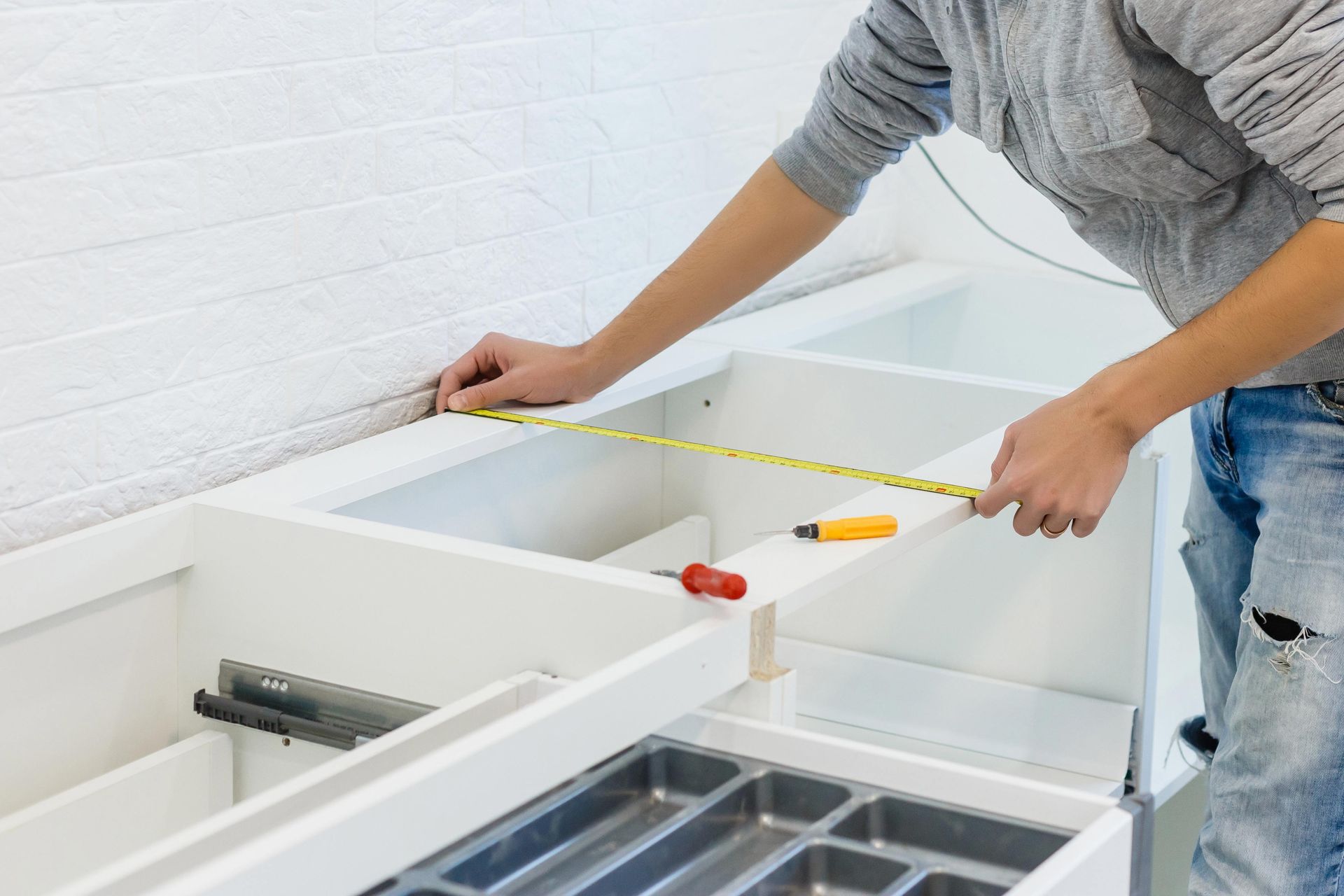 Person measuring a white cabinet frame with a tape measure in a bright room