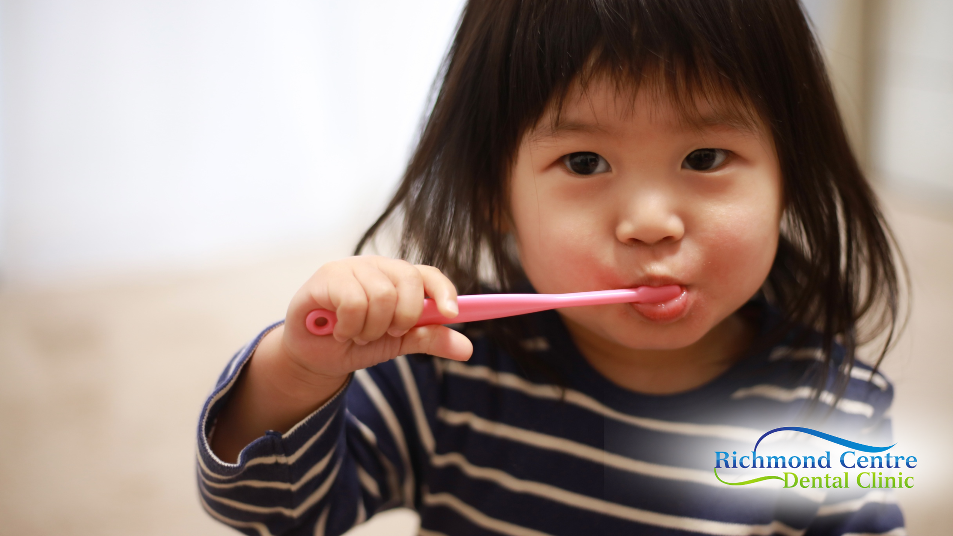 Young child brushing their teeth with a pink toothbrush indoors.