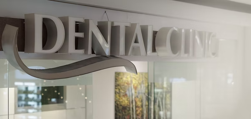 A dental clinic sign is hanging from the ceiling above a glass door.