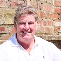 A man in a white shirt is smiling in front of a brick wall.