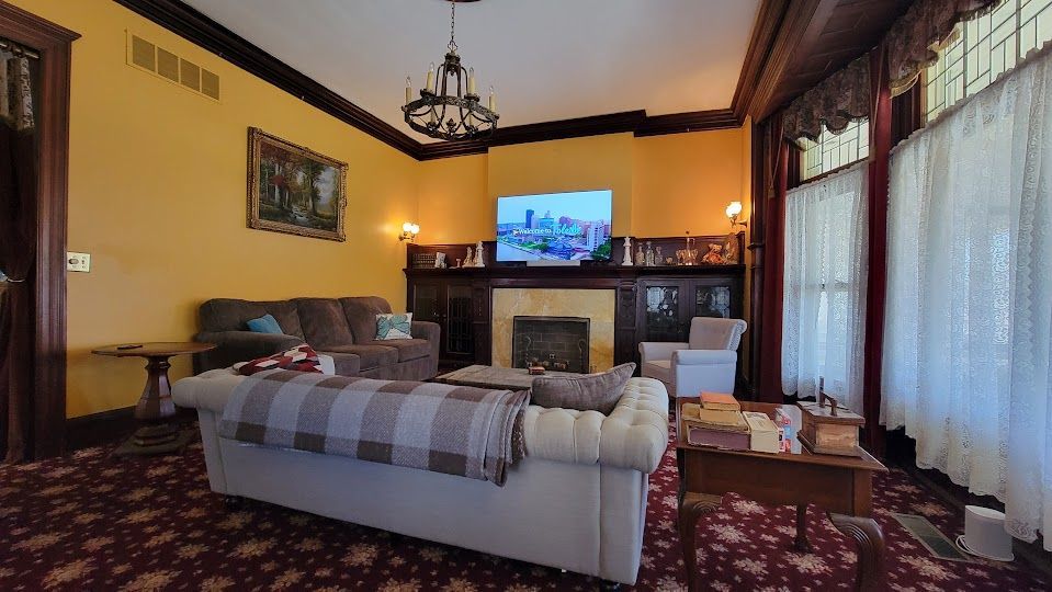 Living room with yellow walls, ornate fireplace, and two sofas, a rug, and a TV.
