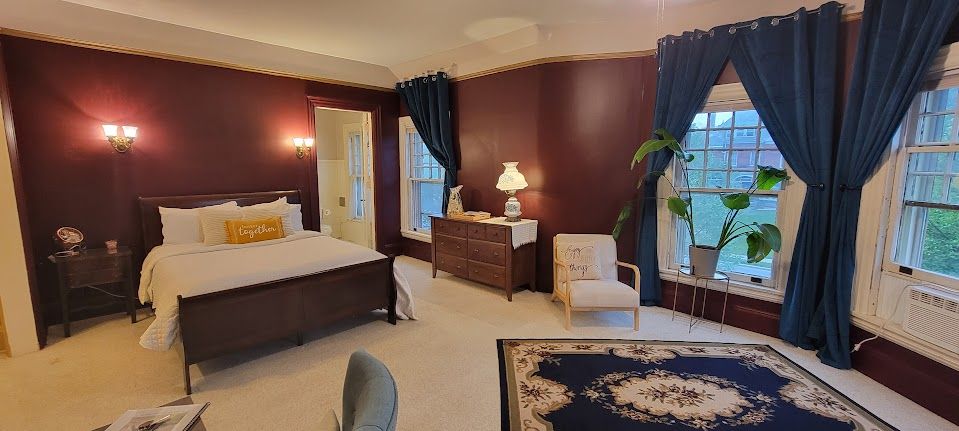 Cozy bedroom with burgundy walls, large windows with blue curtains, and a dark wooden bed.