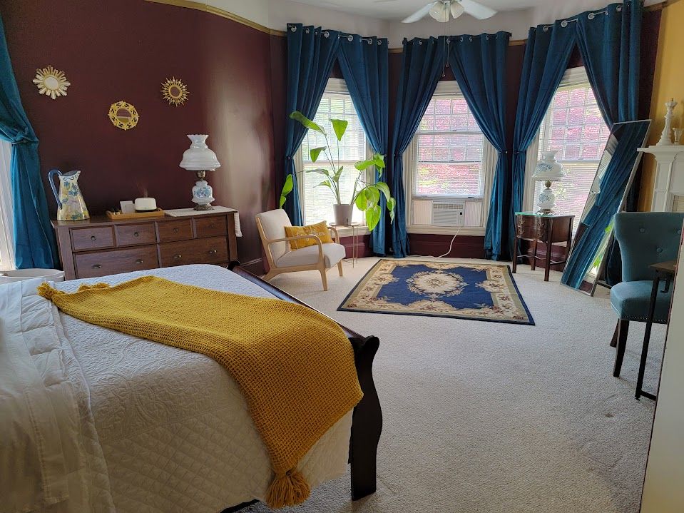 Bedroom with blue curtains, dark red wall, and white bed with yellow throw.