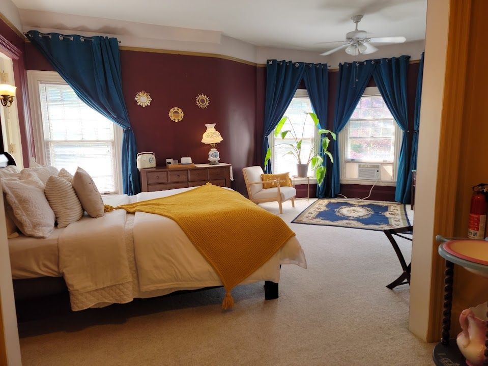 Bedroom with burgundy walls, teal curtains, a bed with yellow blanket, and a rug.